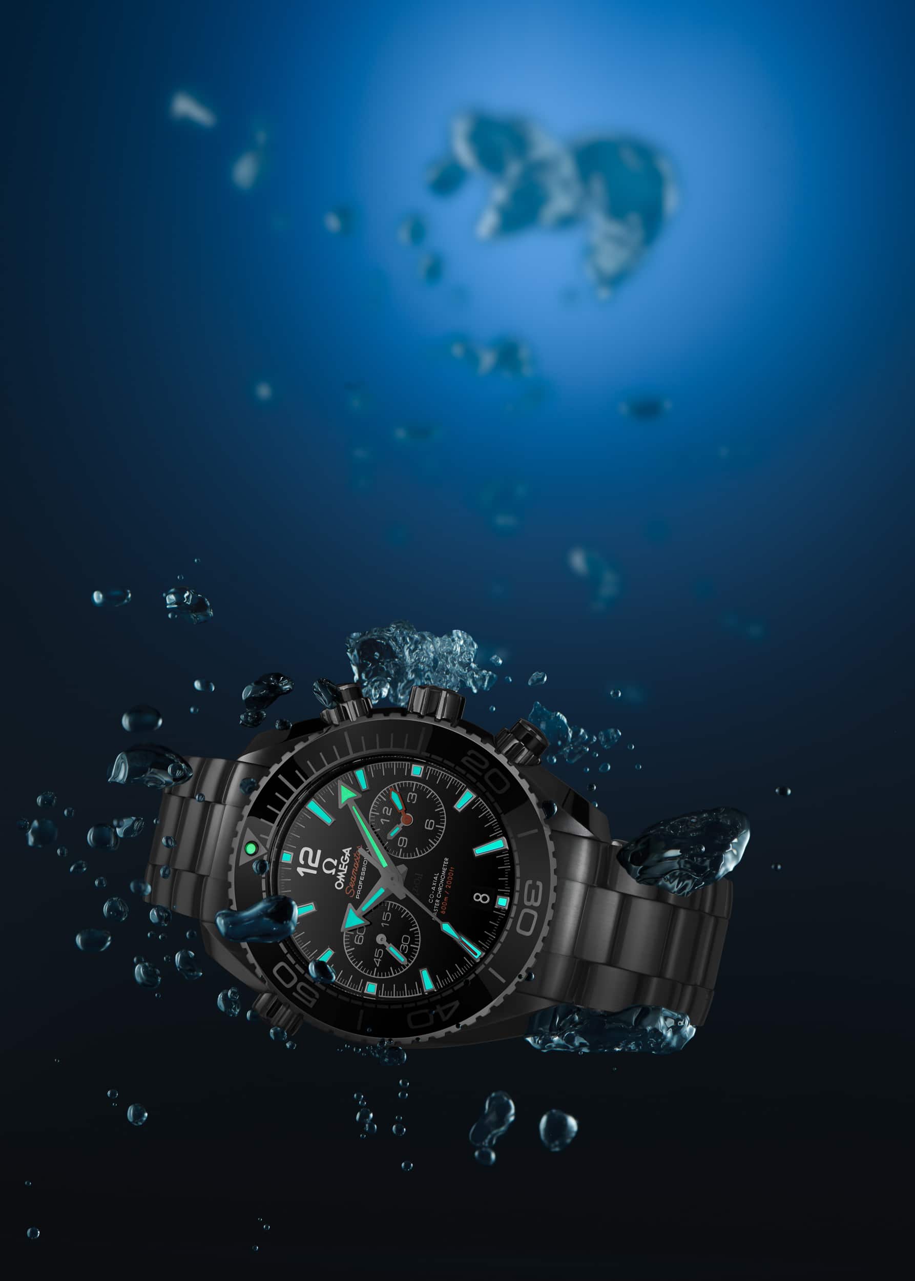 Werbeaufnahme einer Omega Planet Ocean Chronograph 600m Taucheruhr in der Tiefe unter Wasser mit leuchtender Superluminova | Fotograf in der Region Osnabrück Münster Bielefeld für Werbefotografie