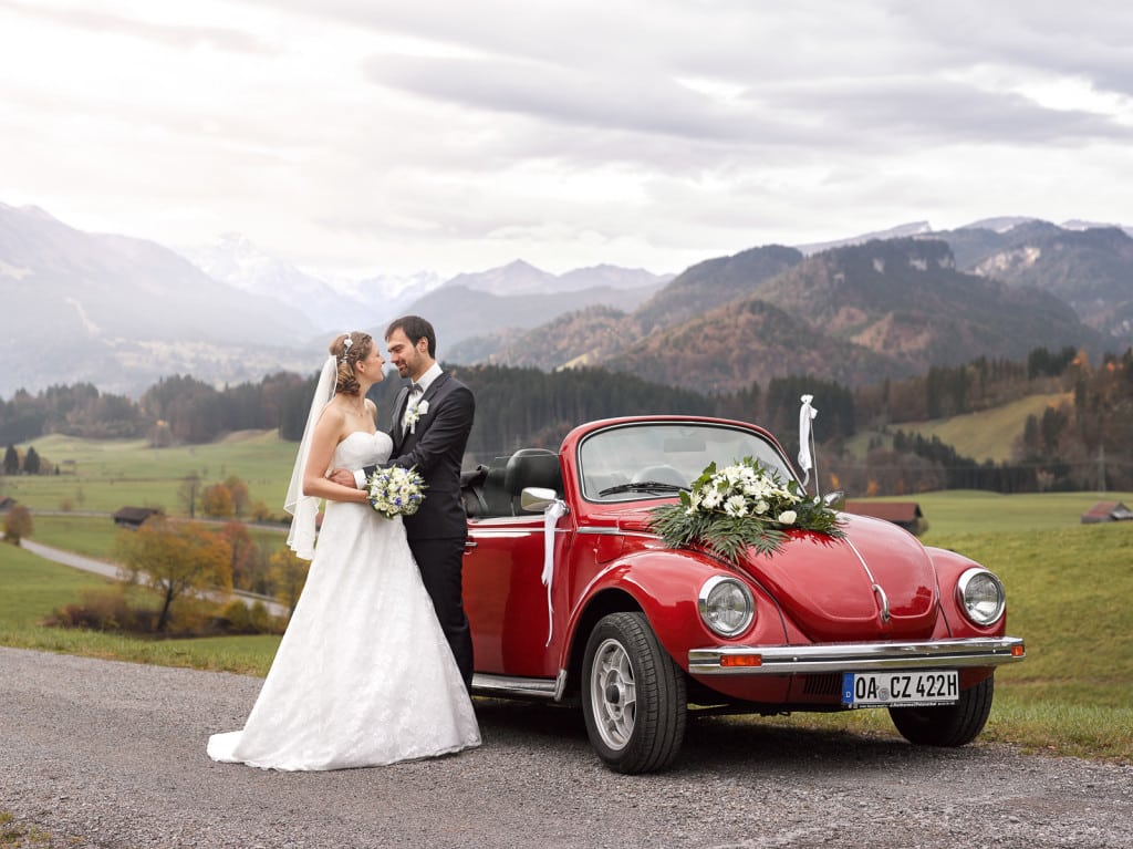 Brautpaar mit VW Käfer Oldtimer vor auf einem Hügel mit den Alpen im Hintergrund | Hochzeitsfotograf im Allgäu Brautpaar mit VW Käfer Oldtimer vor auf einem Hügel mit den Alpen im Hintergrund | Hochzeitsfotograf im Allgäu