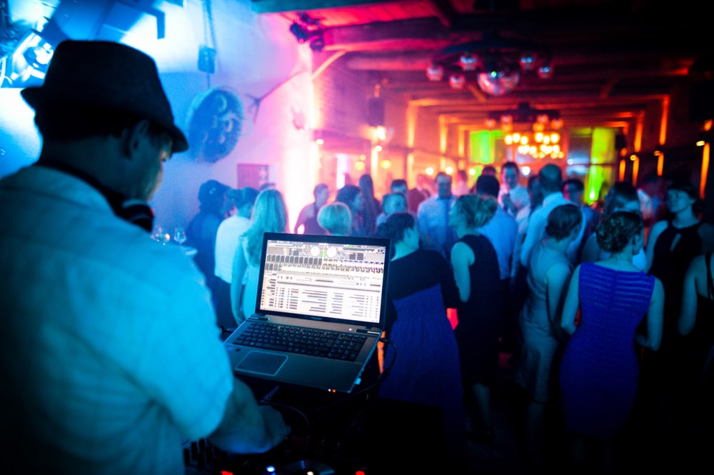 DJ mit Laptop und tanzenden Hochzeitsgästen im Hintergrund